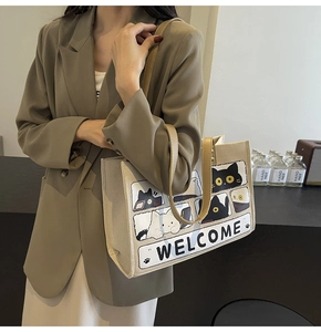 Detail of canvas cat tote bag with cartoon panels held by model in khaki blazer