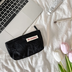 Detail of black nylon makeup bag with bow accent and branded label on white fabric