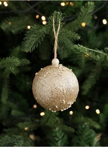 Close-up of golden glitter Christmas ball with white pearl beads on a green pine tree