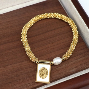 Detail of beaded gold bracelet with Mother Mary medal and white pearl on wood