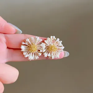 Détail de boucles d'oreilles marguerites avec pétales crème et centre doré texturé