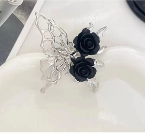 Macro detail of gothic liquid metal butterfly and black rose adjustable ring on a ceramic tray