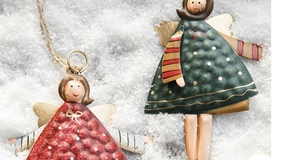 Detail of embossed metal Christmas angel pendant with red and green paint on snowy backdrop