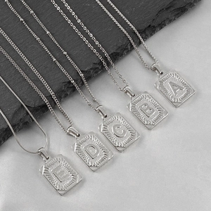 Détail de cinq colliers en acier titane 18K avec pendentifs rectangulaires gravés A à E