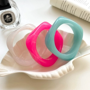 Three square acrylic bangles in pink and blue colors stacked on a white ceramic shell plate
