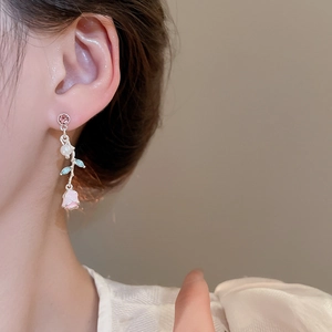 Detail of a pink enamel rose earring with white pearls and blue leaf on a silver branch