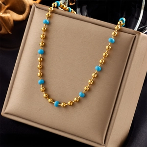 Minimalist gold bead and turquoise beaded necklace presented on a beige jewelry display pad