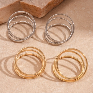Three-layer hollow twisted round earrings in gold and silver finish on stone background