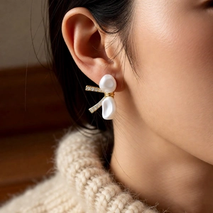 Detailed close-up of a pearl bow earring with gold plating and zircons worn on ear