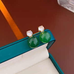Vue macro de boucles d'oreilles dorées avec perles et pierres vertes sur un écrin