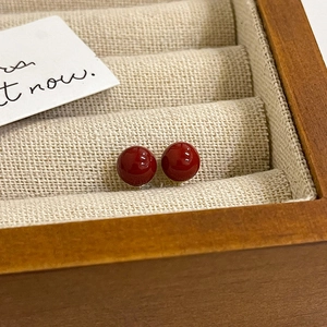Macro view of minimalist red pearl stud earrings resting in a premium wooden jewelry box