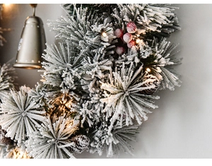 Close-up of frosted Christmas wreath with red berries, pine cones and golden bell