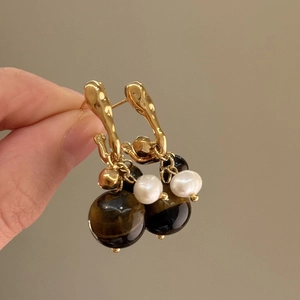 Macro detail of gold-plated geometric earrings with tiger eye stone and white pearl