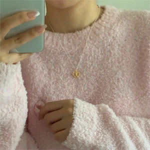 Close-up of a delicate golden heart necklace worn with a cozy pink knitted sweater