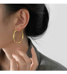 Close-up of a model wearing gold geometric twisted hoop earrings with a metallic finish