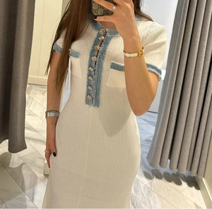 Detail of white knit mini dress featuring blue trim and elegant gold buttons
