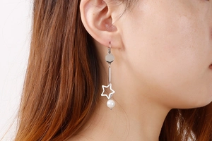 Détail de boucles d'oreilles pendantes argentées avec étoile et perle sur mannequin