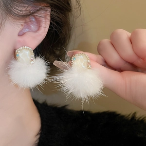 Detail of white fluffy pompom earrings with gold edges and sparkling rhinestones
