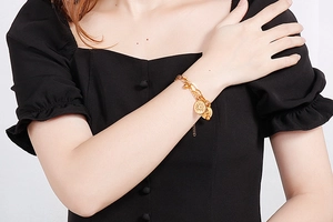 Detail of gold double-layer chain bracelet featuring sunburst and disc pendants