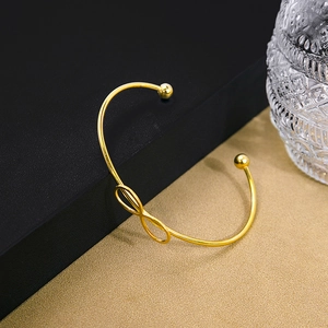 Detail view of a gold knot cuff bracelet with an infinity symbol on a textured surface
