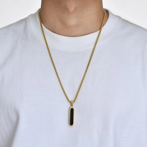 Close-up of geometric black octagon pendant on a golden box chain worn by a male model