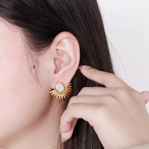 Détail de boucles d'oreilles soleil dorées avec pierre blanche portées par un mannequin