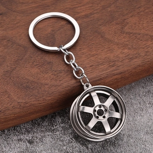 Macro shot of a 6-spoke silver car wheel rim keychain on a wooden and stone surface