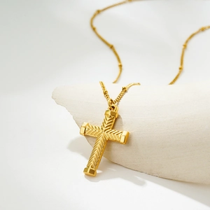 Detail shot of golden stainless steel cross pendant with herringbone texture on stone base