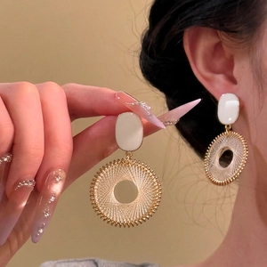 Close-up of large round drop earrings featuring intricate white woven radial texture