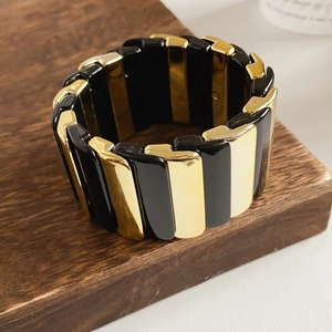 Detail of the black and gold geometric stretch bracelet on a brown wood base