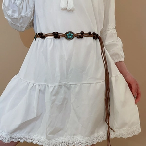 Detail of bohemian brown woven belt with wooden beads and turquoise flower buckle on white dress