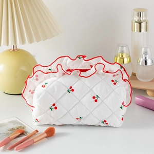 Détail d'une trousse à maquillage matelassée à motif cerise avec bords à volants rouges
