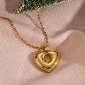 Detail of 18K gold-plated heart necklace on beige silk fabric with green pine needle