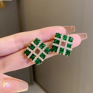 Macro view of gold square earrings featuring emerald stones and sparkling crystal pavé