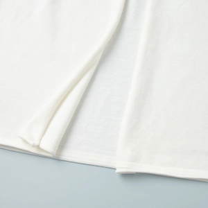 Detailed close-up of white knitted cardigan hem with smooth split seam finishing