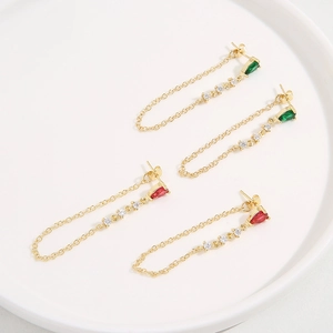 Flat lay of gold chain tassel earrings with green and red teardrop gems on a white plate