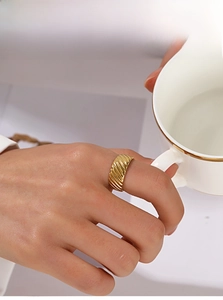 Detail of a golden croissant ring with a twisted texture worn while holding a teacup