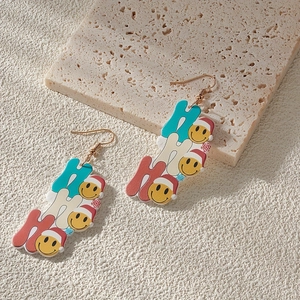 Close-up of Ho Ho Ho Christmas earrings with smiley faces and Santa hats on acrylic material