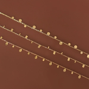 Three minimalist gold titanium steel necklaces with geometric charms on a dark red base