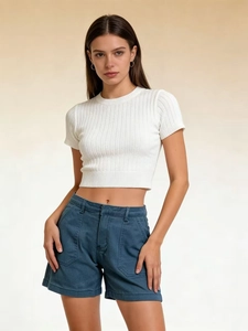 Vista frontale di crop top bianco in maglia e pantaloncini di jeans blu a vita alta