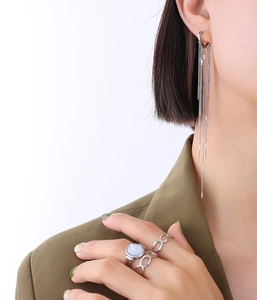 Detail of elegant silver tassel chain earrings and minimalist gemstone rings on model