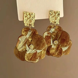 Detailed view of amber acrylic floral earrings with hammered golden metal square studs