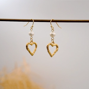 Golden hammered heart earrings with freshwater pearls hanging on a minimalist display stand