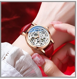 Close-up of gold ladies mechanical watch with red leather strap and skeleton dial