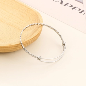 Close-up of a silver twisted cable bangle with adjustable sliding knot on wood tray