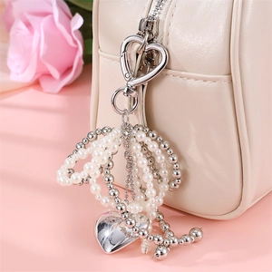 Elegant white pearl heart keychain with silver charms on a beige designer handbag