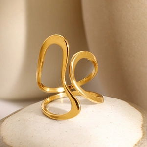 Macro shot of polished 18k gold irregular wavy line ring on a textured stone surface