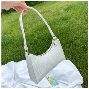 Detail of white crocodile pattern underarm bag with gold zipper on a lawn background
