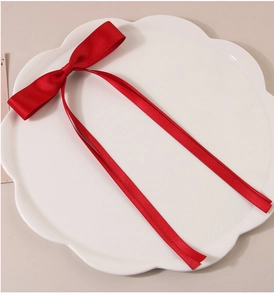Detail of red satin ribbon bow hair clip on a white decorative plate