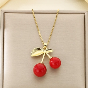 Detailed view of a gold cherry pendant necklace with red round charms in a jewelry box